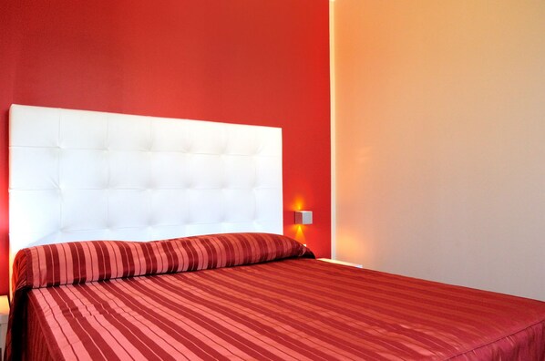 Une chambre d’hôtel avec une tête de lit blanche à motifs capitonnés, une couvre-lit à rayures rouges et un mur d’accent rouge.