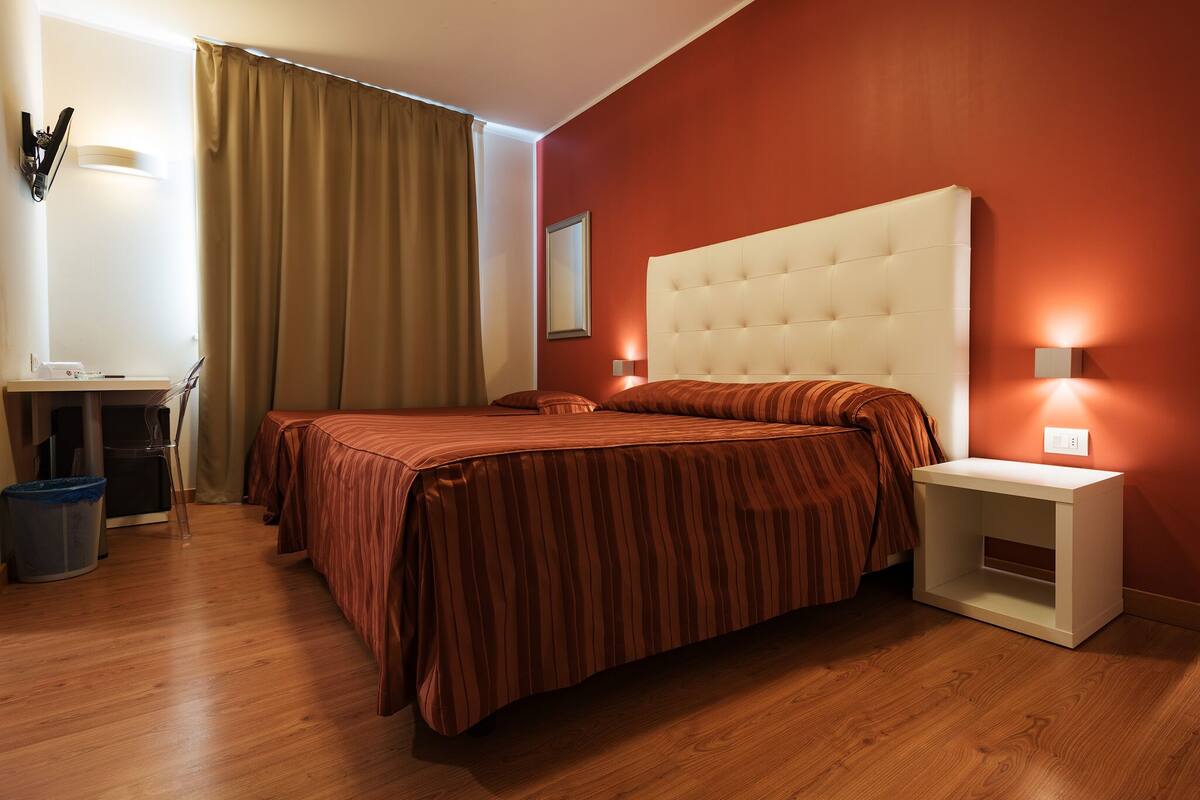 A hotel room with a large bed, a bedside table, a desk, and a chair.