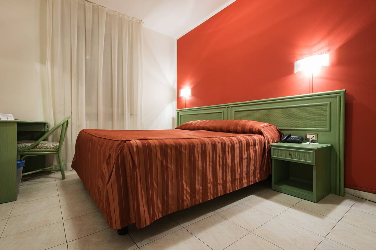 A room with a bed, a nightstand, a chair, and a desk.