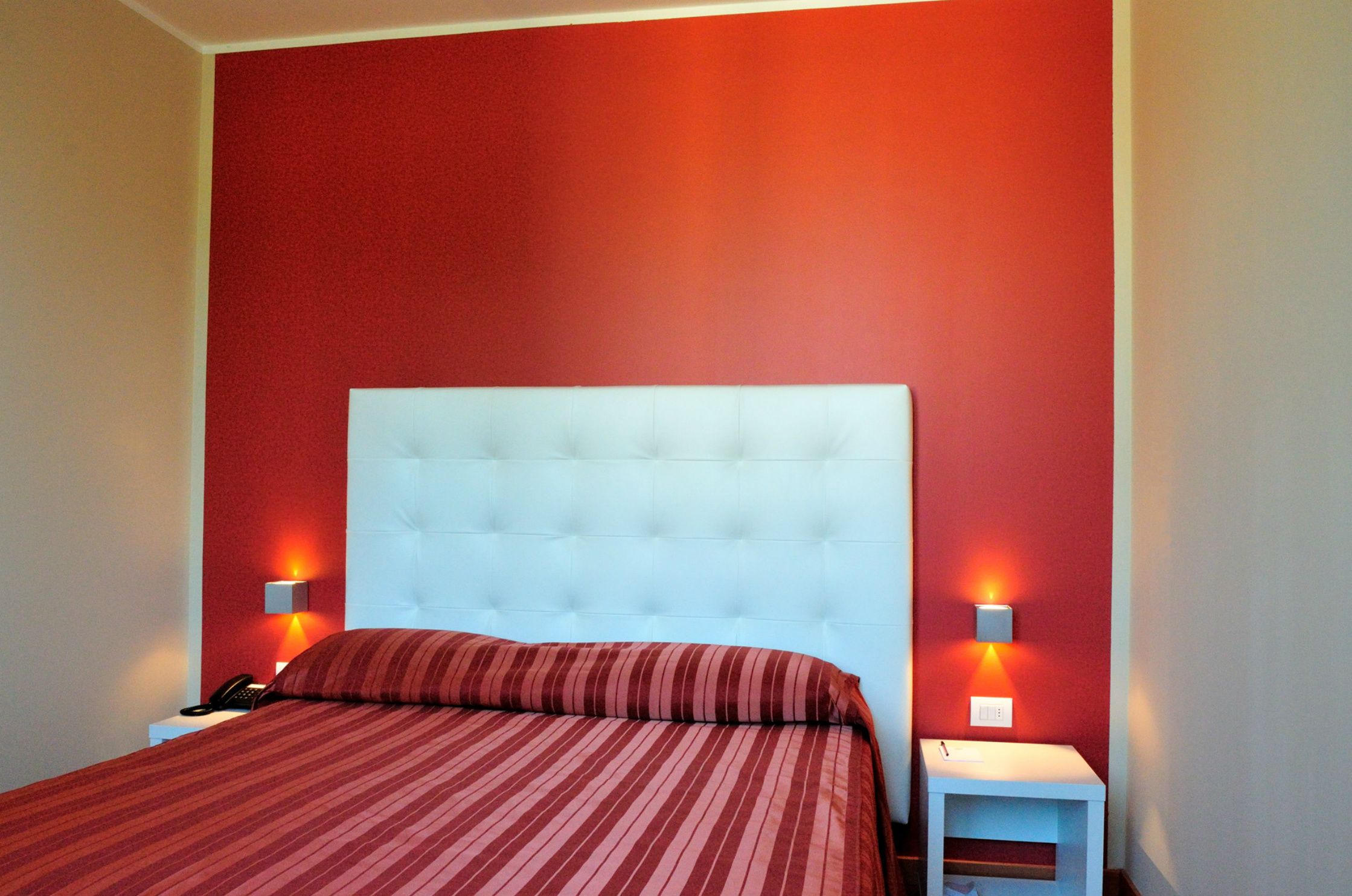 Una habitación de hotel con una cama grande, paredes rojas y dos lámparas de noche.