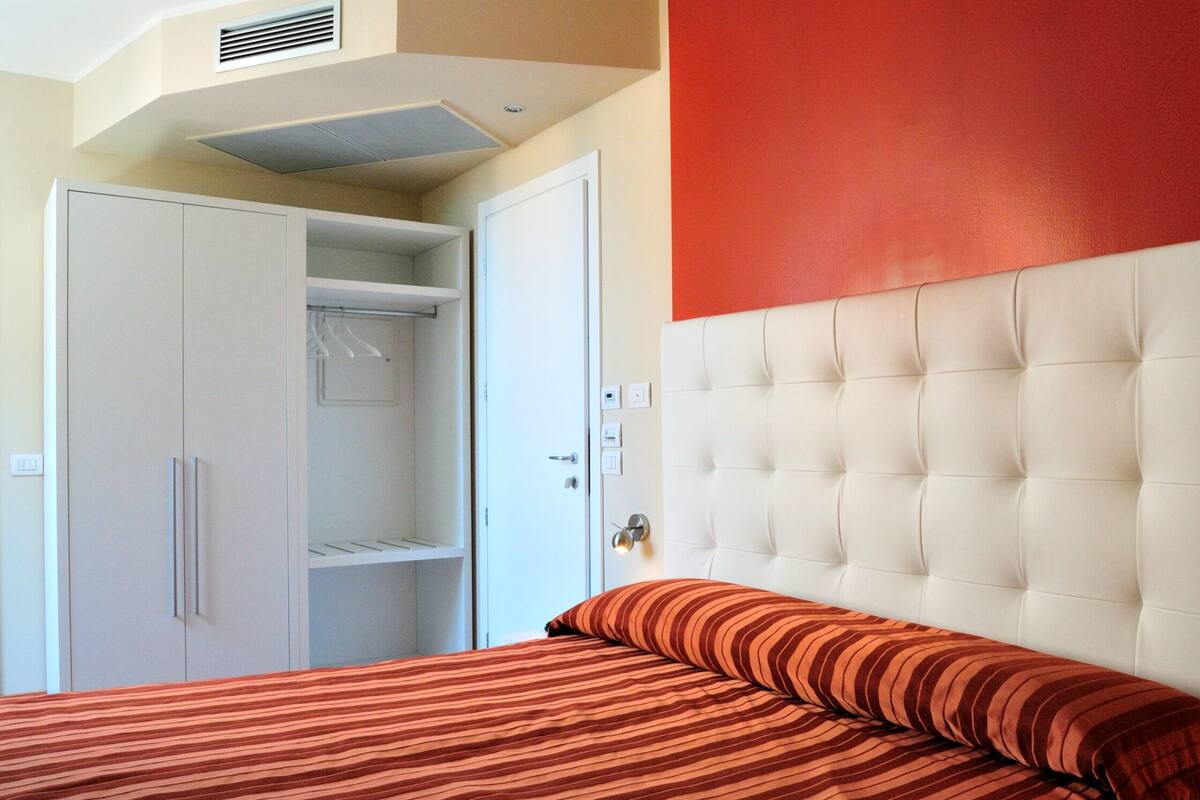 A bedroom with a bed, a wardrobe, and a red accent wall.