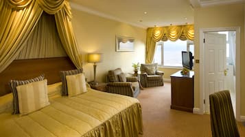 A hotel room with a large bed, a television, a desk with a fruit bowl, and a view of the ocean.