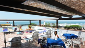Una terraza con vistas al mar, con sillones, mesas y una zona de piscina.