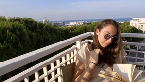 Iemand leest een boek op een balkon met uitzicht op een vuurtoren en groen.
