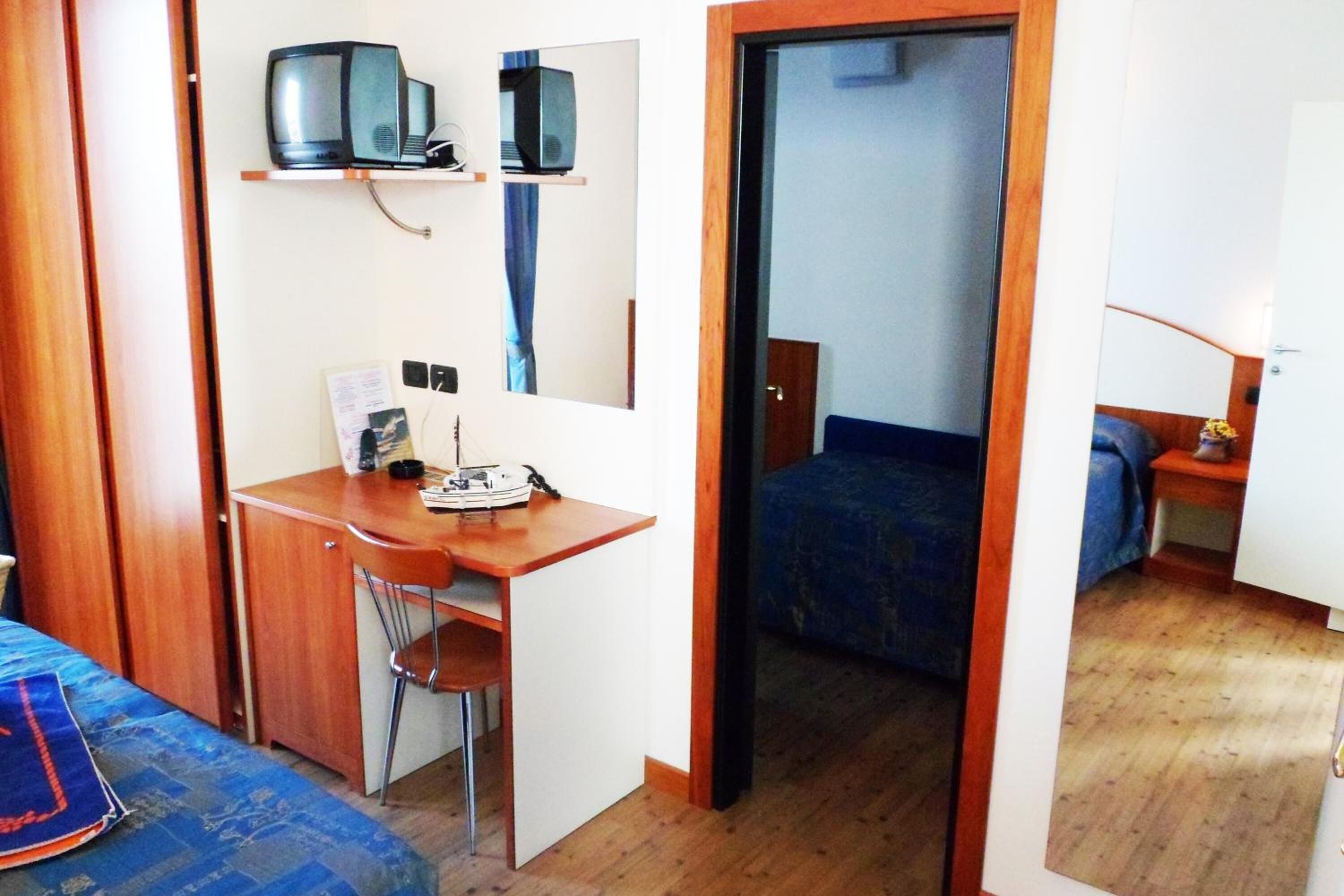 Habitación pequeña con cama, escritorio y silla. Se ve una puerta que conduce a otra habitación.