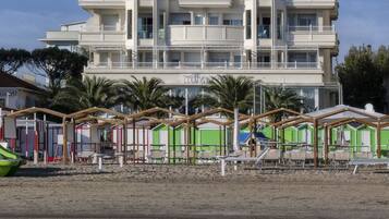 Un hotel de varios pisos con balcones, cerca de una playa con cabañas de playa.