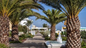A paved pathway flanked by palm trees leading to a building with a sign that reads "Hotel de la Playa." - Tiffany's (Riccione)