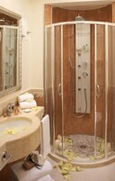 A bathroom with a glass-enclosed shower, a sink with a mirror, and a bathtub with rose petals.