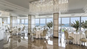 A spacious dining area with tables set for a meal, large windows offering a view of the sea, and a modern chandelier. - Tiffany's (Riccione)