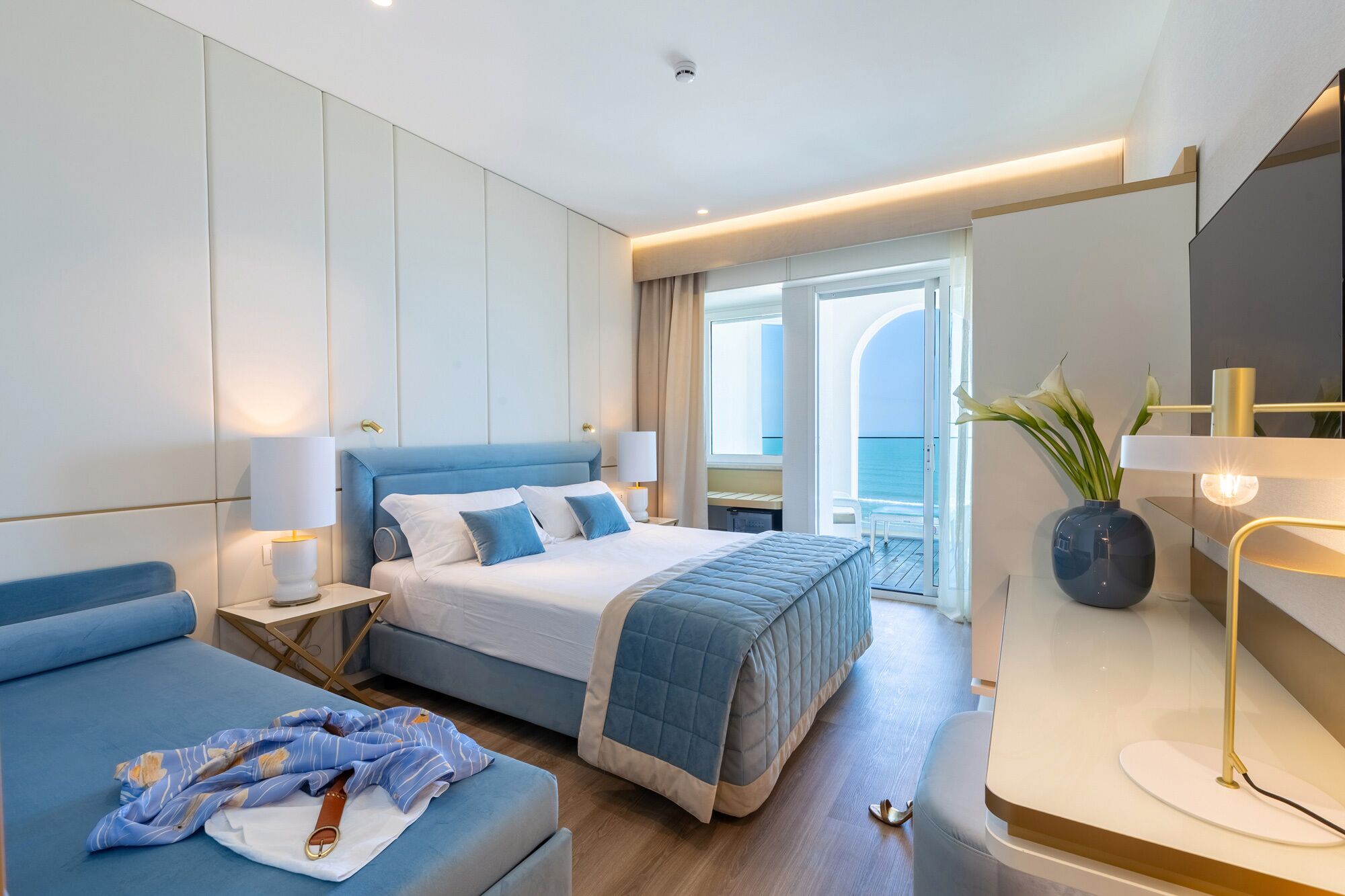 Habitación de hotel moderna con una cama grande, una zona de estar, un escritorio y vistas al mar.