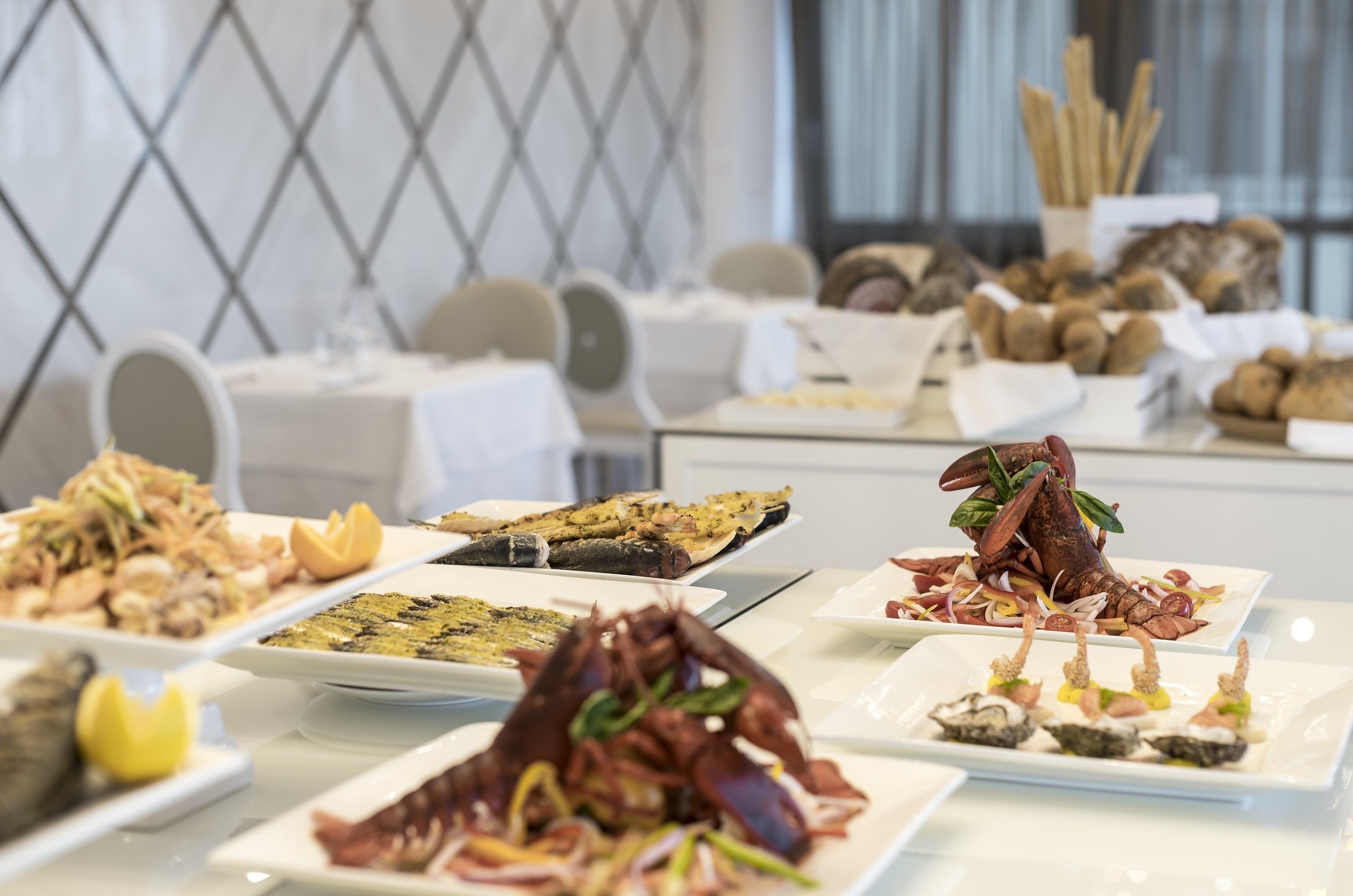 Una mesa de bufé con diversos platos, entre ellos mariscos y aperitivos, en un comedor moderno con un diseño geométrico en la pared.