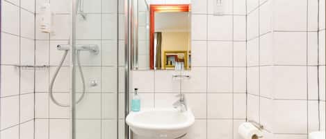 Un baño con cabina de ducha de vidrio, un lavabo blanco con espejo y un inodoro con dispensador de toallas de papel.