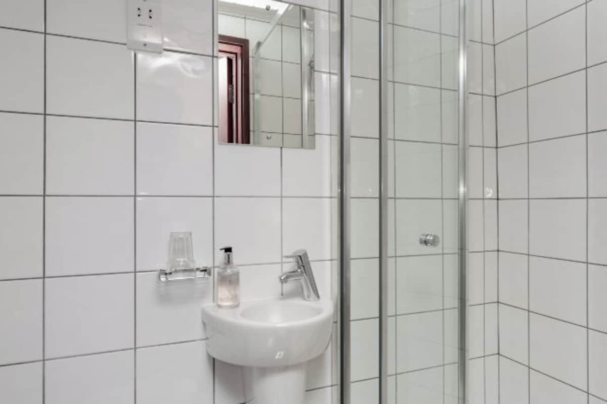 A bathroom with white tiled walls, a sink with a mirror above it, and a glass shower enclosure.