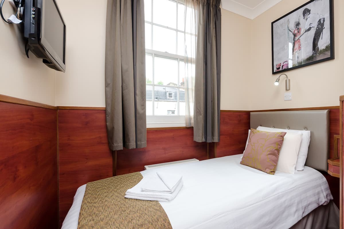 Una habitación de hotel con cama, televisión, ventana con cortinas y un cuadro en la pared.
