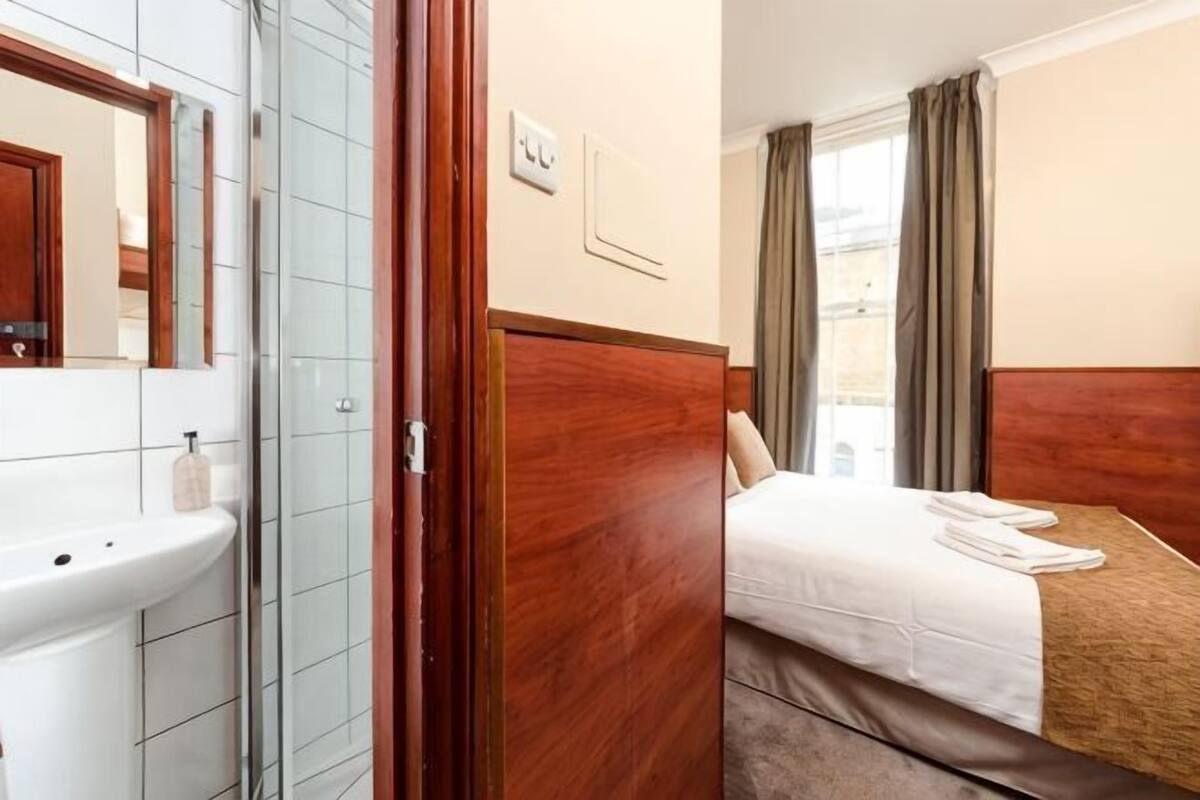 A hotel room with a bathroom, a bed, a window, and a view of the city.