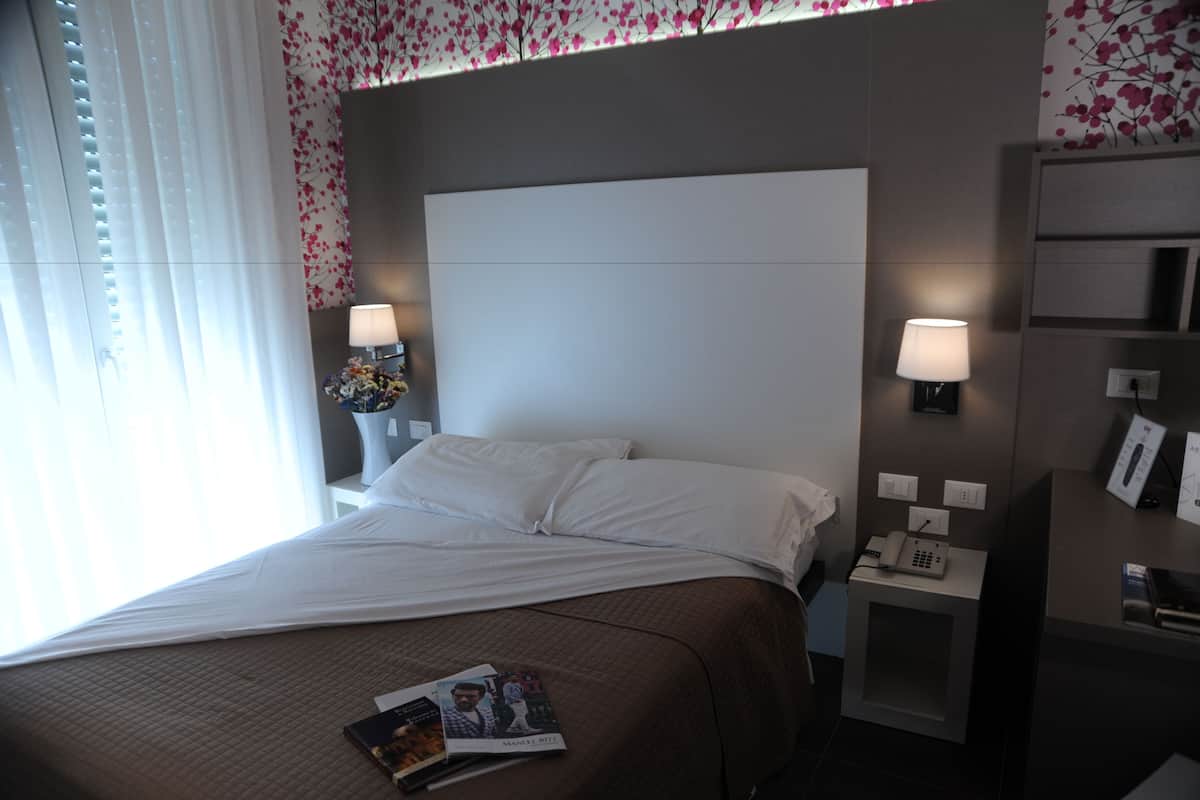 Ein Hotelzimmer mit einem großen Bett, zwei Nachttischen mit Lampen, einem Beistelltisch mit Telefon und einer Wand mit floralem Muster.