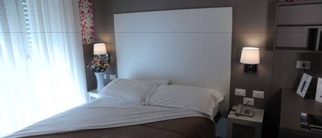 Habitación de hotel con una cama grande, dos mesitas de noche con lámparas, una mesita auxiliar con teléfono y un papel tapiz estampado con flores.