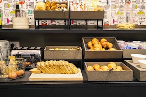 Un buffet proposant une variété d’aliments, notamment du pain, des pâtisseries et des condiments.