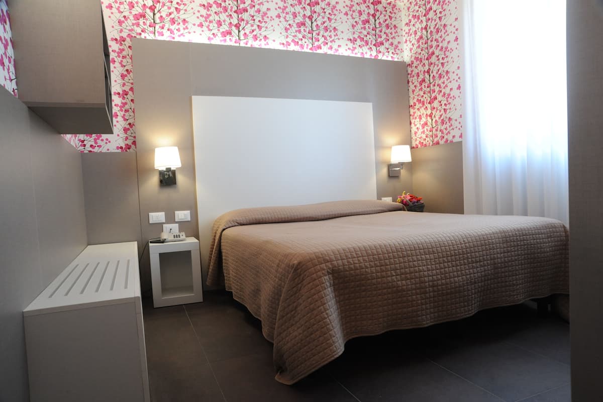 Ein Hotelzimmer mit einem großen Bett, zwei Nachttischen, einer Wandlampe und einem Vorhang mit Blumenmuster.