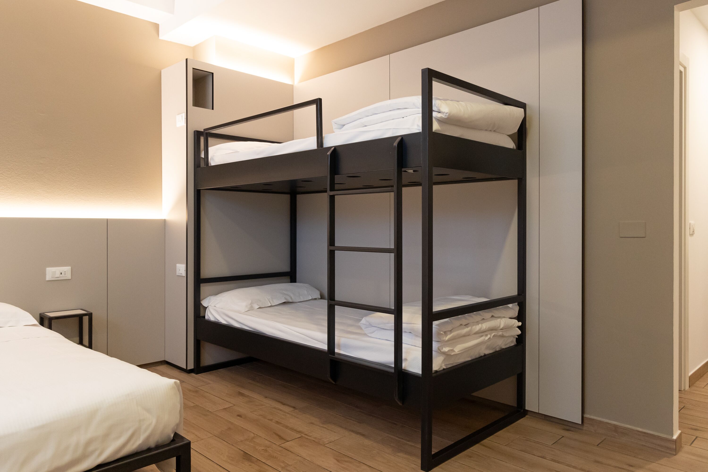 A bunk bed with white bedding in a room with wooden flooring and a small bedside table.