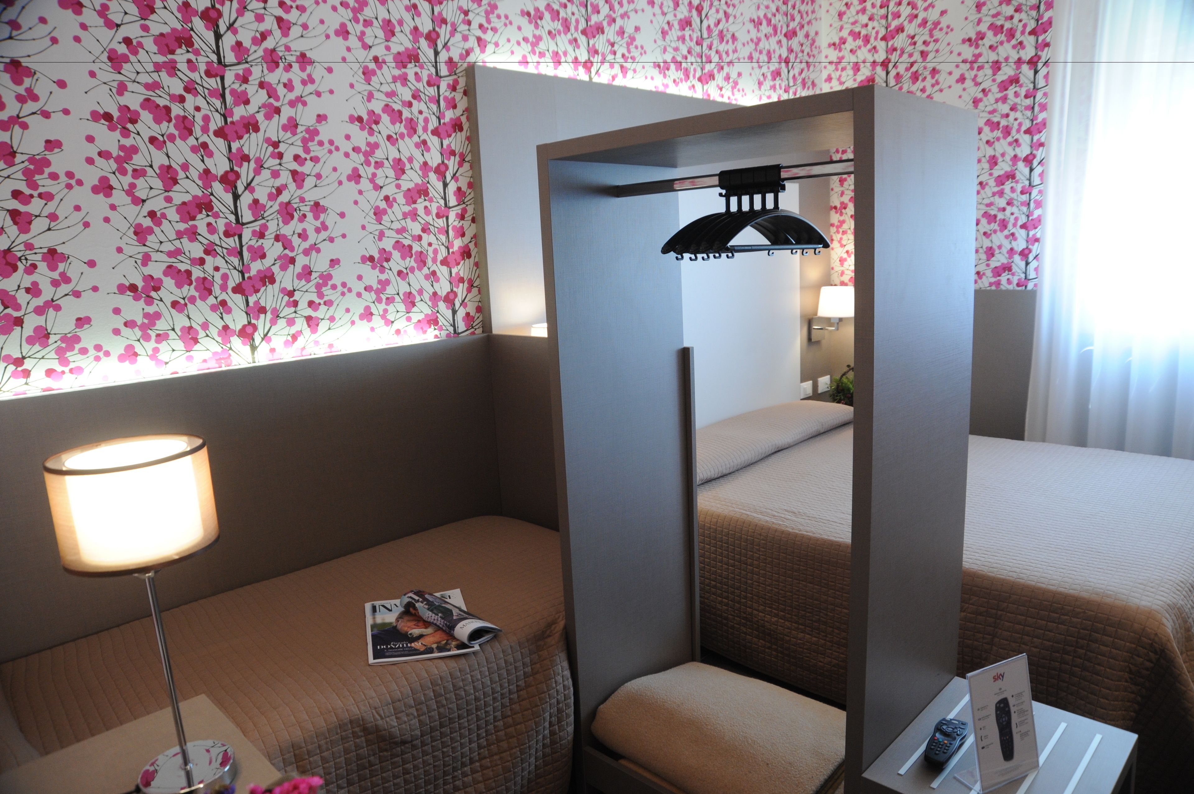 Une chambre d’hôtel avec un lit, une table de chevet avec une lampe, un magazine et un petit coin salon avec un coussin.