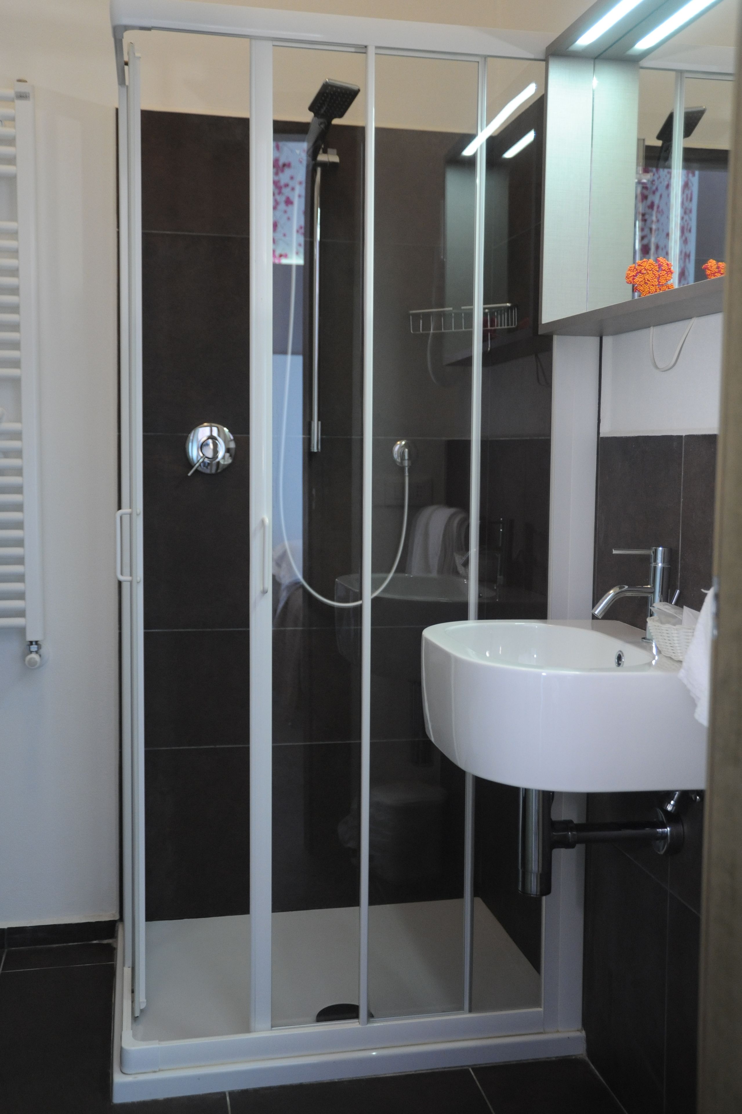 A modern bathroom with a glass-enclosed shower, a white sink, and dark tiled walls.