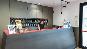 Balcão de receção com uma mulher atrás, exposição de sapatos e placa a indicar zona para fumadores.