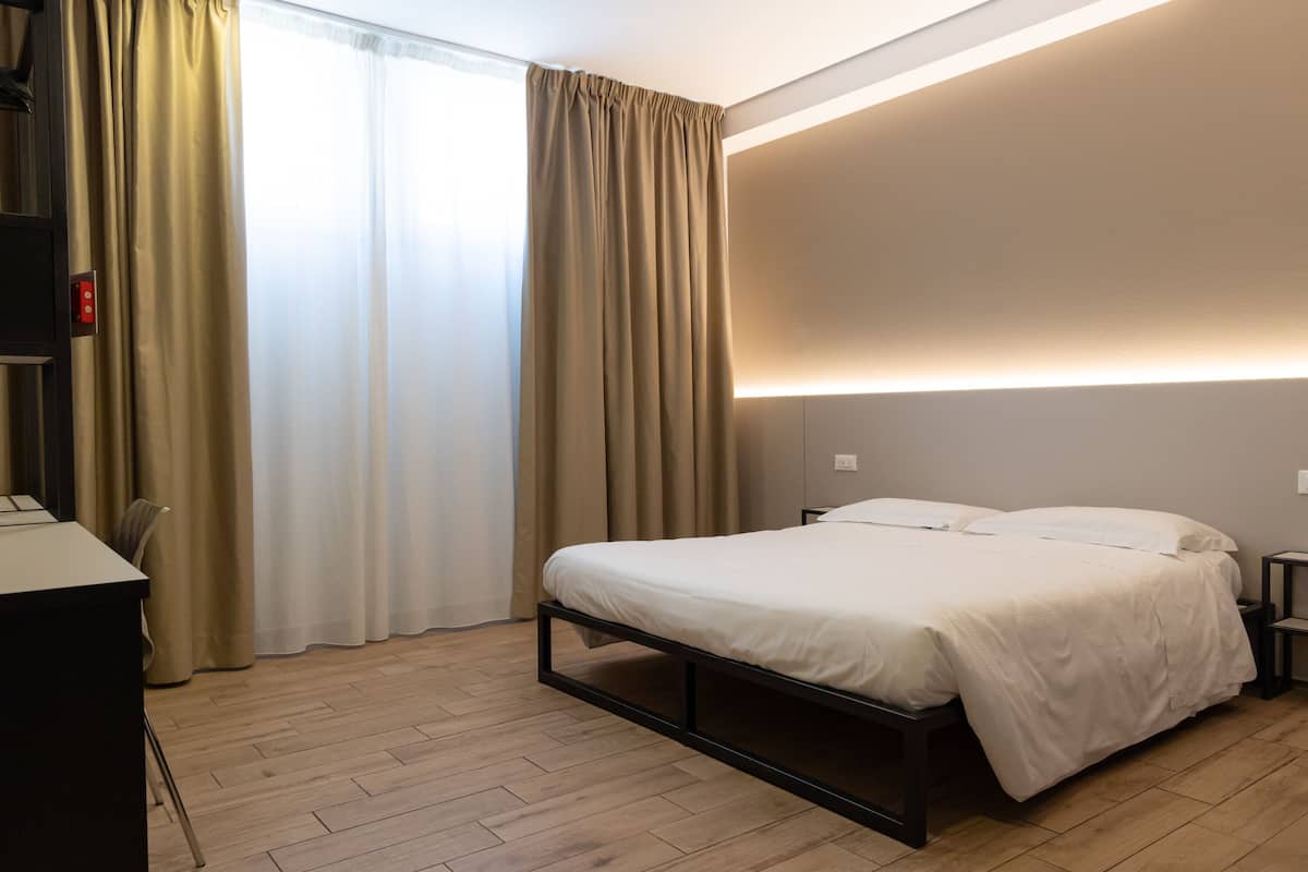 Ein modernes Hotelzimmer mit Bett, Nachttischen, Schreibtisch und einem fenster mit Vorhängen.
