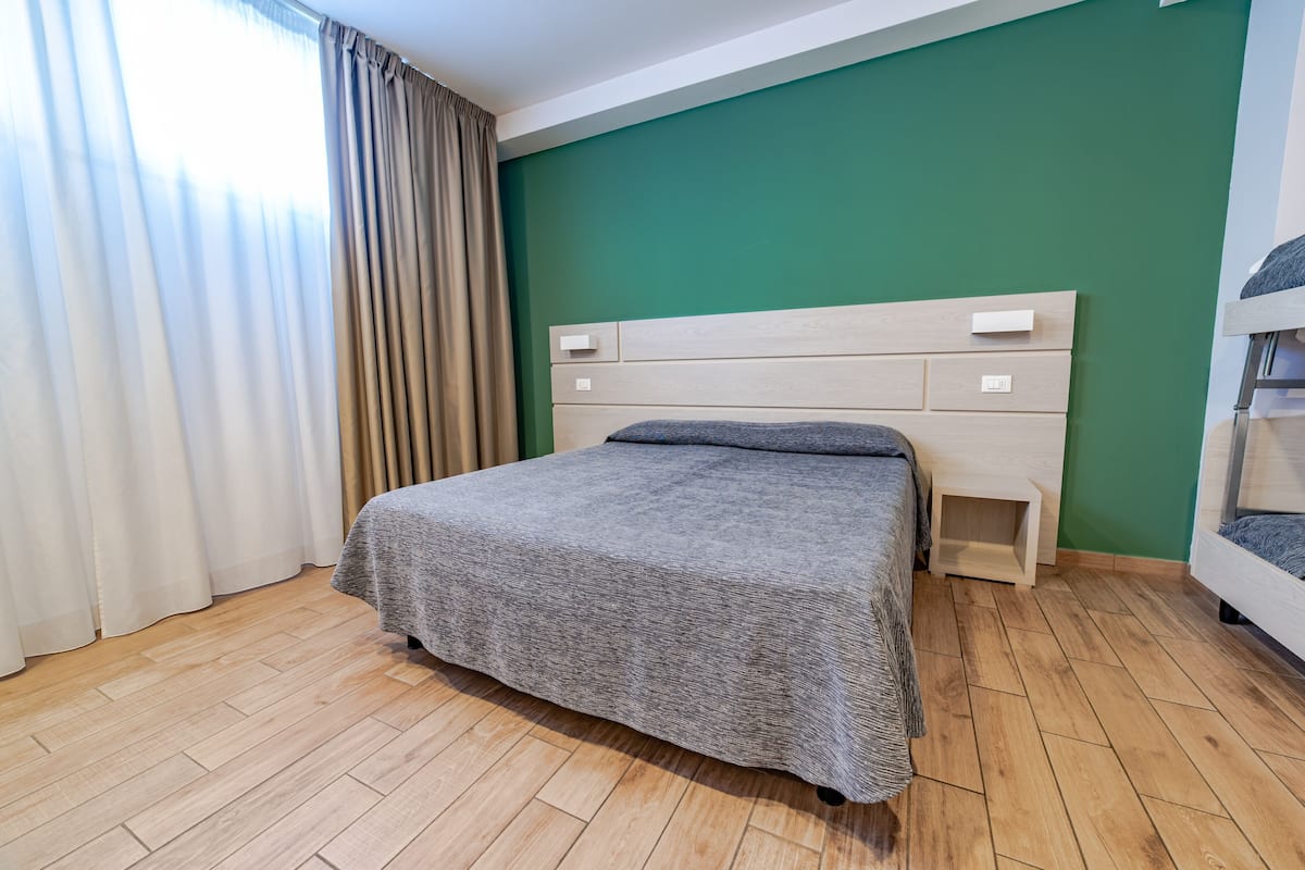 Ein ordentlich bezogenes Bett in einem Zimmer mit grüner Wand und Holzboden.