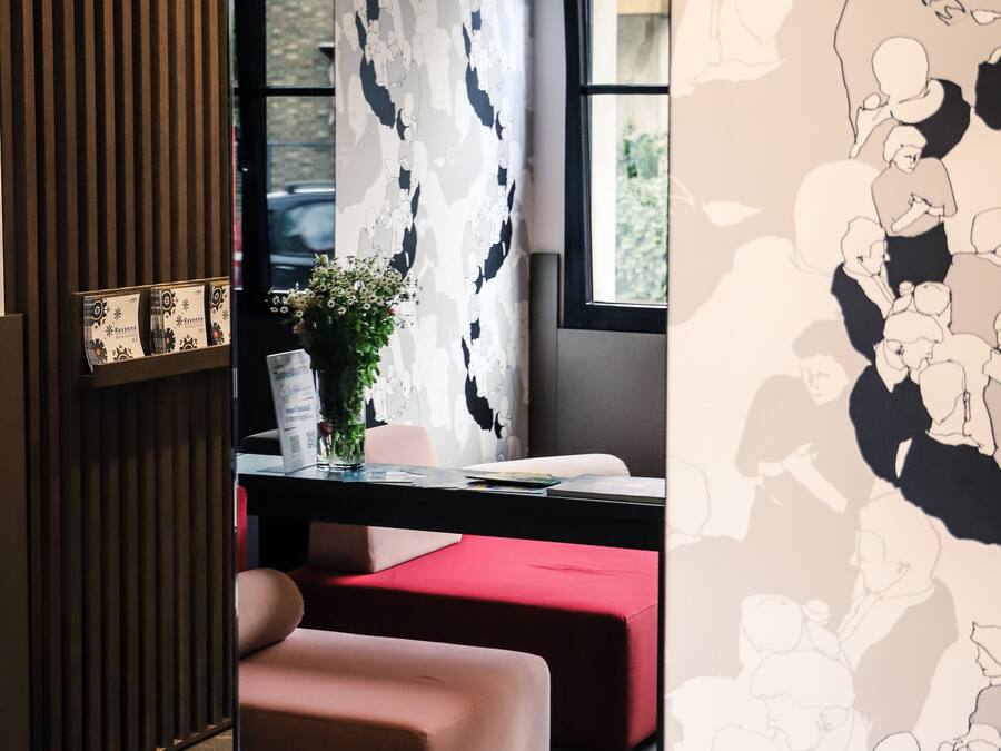 Quarto moderno com parede de ripas de madeira, papel de parede estampado, escrivaninha com um vaso de flores e um banco acolchoado vermelho.