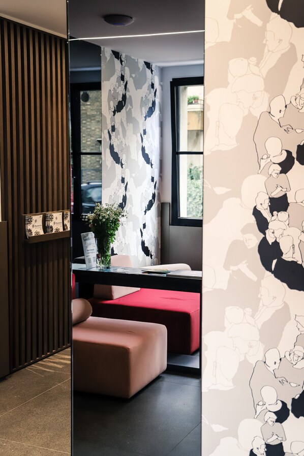 A modern room with a wooden slat wall, a patterned wallpaper, a desk with a vase of flowers, and a red cushioned bench. - Astoria (Ravenna)