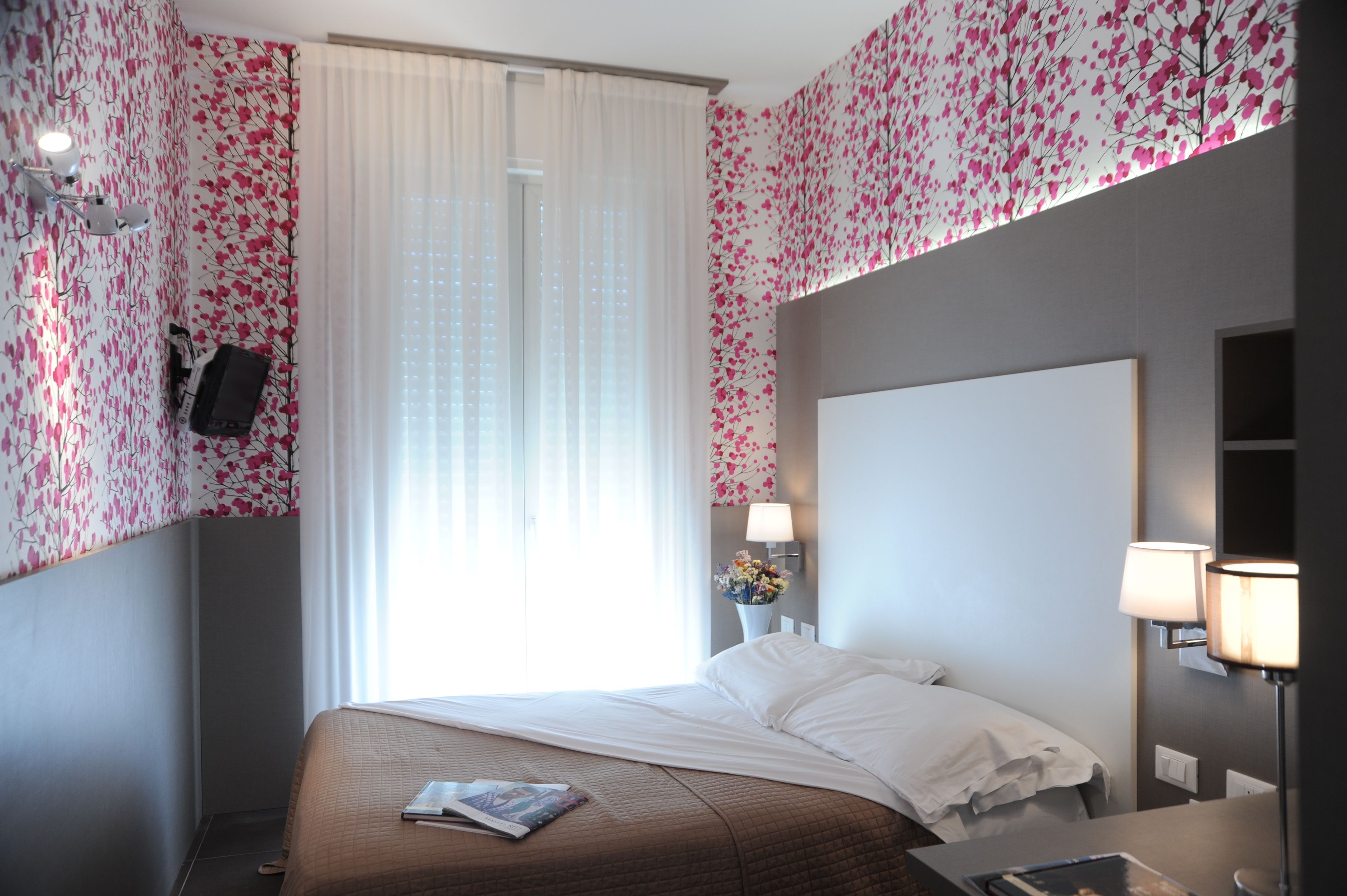 A hotel room with a large bed, a bedside table, a lamp, and a wall-mounted TV.