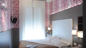 Ein Hotelzimmer mit einem großen Bett, einem Nachttisch, einer Lampe und einem am Wand montierten Fernseher.