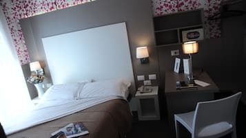 Habitación de hotel con una cama grande, lámparas de noche, un escritorio con teléfono y una silla.