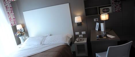 A hotel room with a large bed, bedside lamps, a desk with a telephone, and a chair.