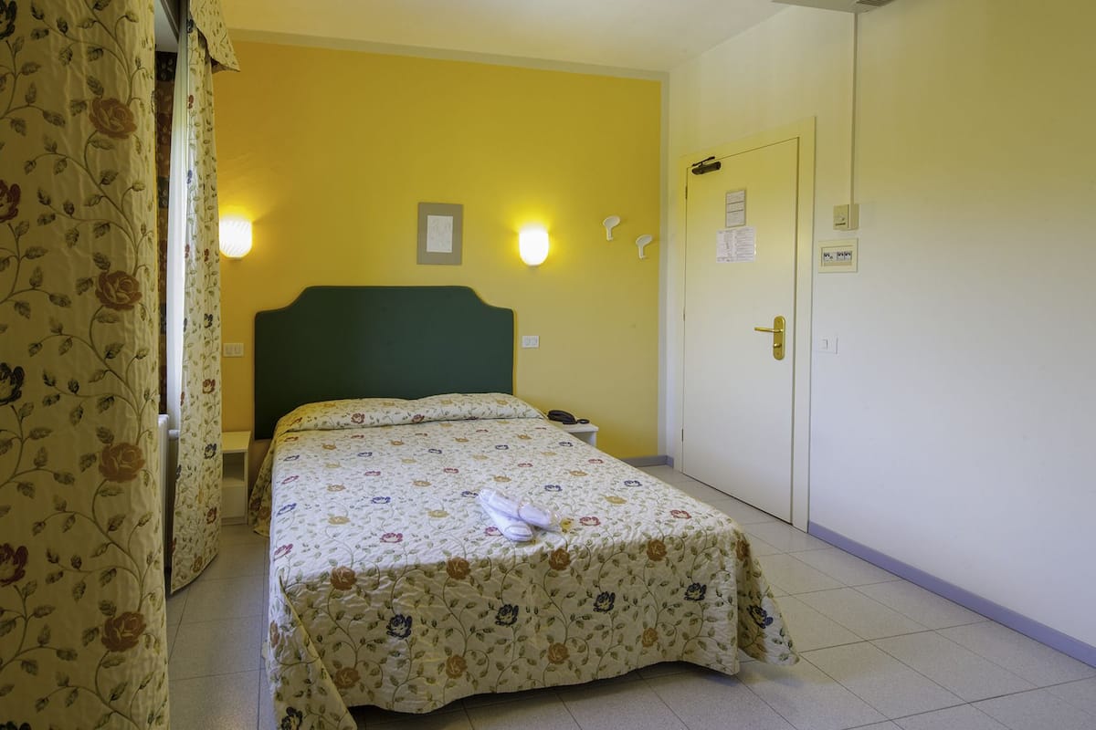 Ein Hotelzimmer mit Bett, Nachttisch, Tür und Wand mit einer Leuchte.
