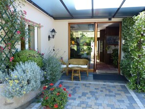 Un patio techado con una mesa y sillas de mimbre, rodeado de plantas y flores.