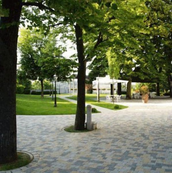 Une cour dallée, agrémentée d’arbres, avec une structure blanche en arrière-plan.