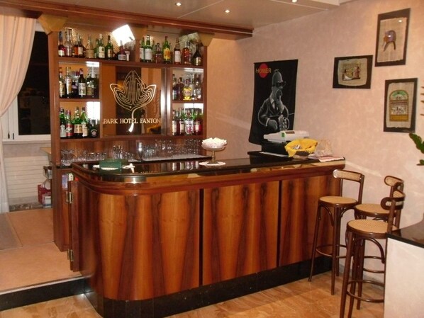 Zona de bar con mostrador de madera, estantes llenos de botellas de licor y cuadros en la pared.