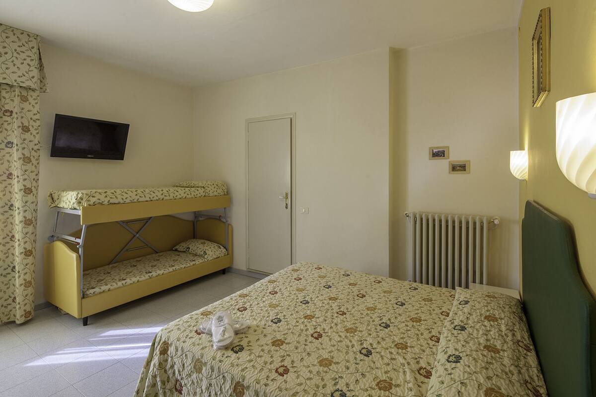 Ein Zimmer mit einem Etagenbett, einem Einzelbett, einem Heizkörper, einem Fernseher und einer Tür.