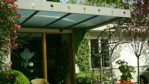 Un espace extérieur abrité comprenant une chaise, des plantes en pot et l’entrée d’un bâtiment.