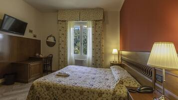 Ein Hotelzimmer mit Bett, Schreibtisch, Stuhl, Fernseher, einem Fenster mit Vorhängen und einer Lampe.