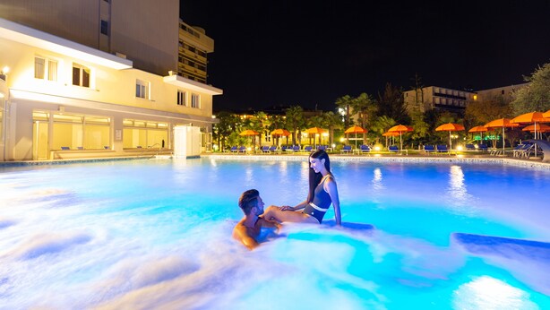 A swimming pool with a couple in the water, surrounded by lounge chairs and umbrellas. - Hotel Savoia Thermae & Spa (Abano Terme)