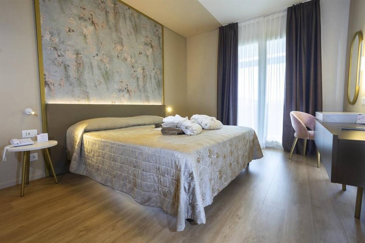 Une chambre d’hôtel avec un grand lit, un bureau, une chaise et un grand tableau abstrait accroché au mur.