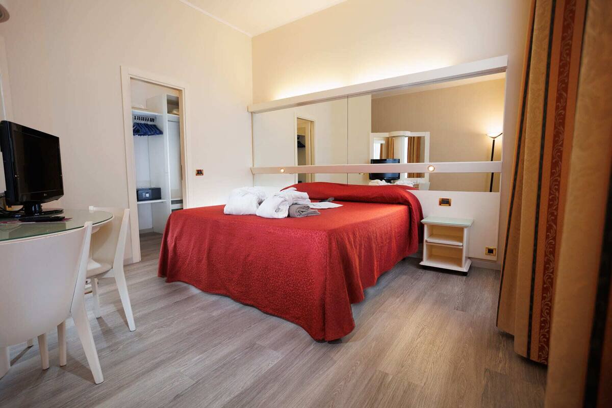Une chambre d’hôtel équipée d’un lit, d’un bureau, d’une télévision et d’un miroir.
