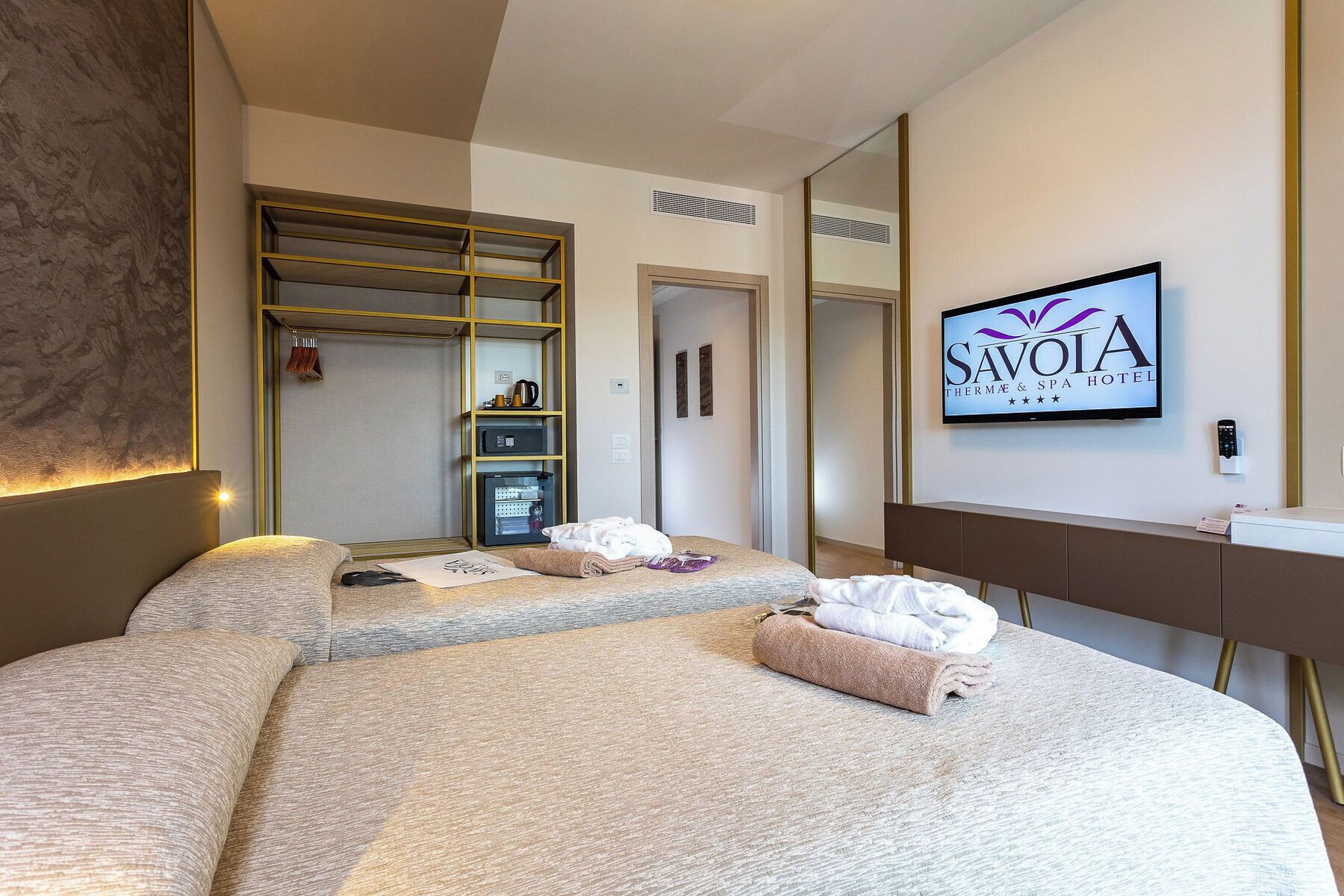 A hotel room with a bed, a bedside table, a TV, a mirror, and a wardrobe.