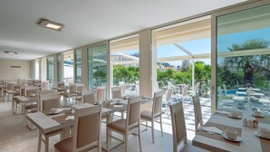 A spacious indoor dining area with large windows overlooking a pool and greenery. Tables are neatly arranged with chairs, and the room has a modern, clean design. - Hotel Savoia Thermae & Spa (Abano Terme)