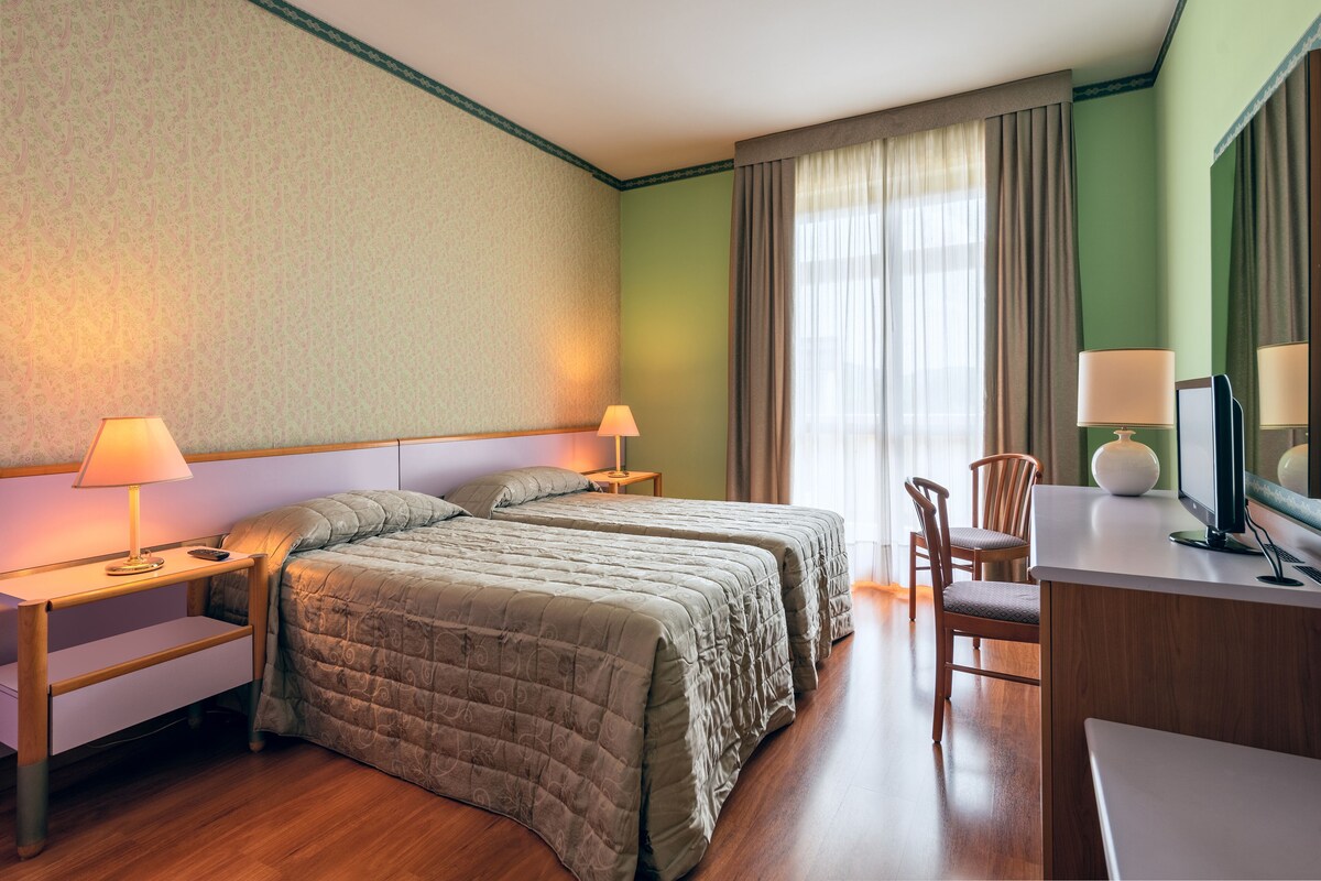 Une chambre d’hôtel avec deux lits, un bureau, une chaise et un téléviseur.
