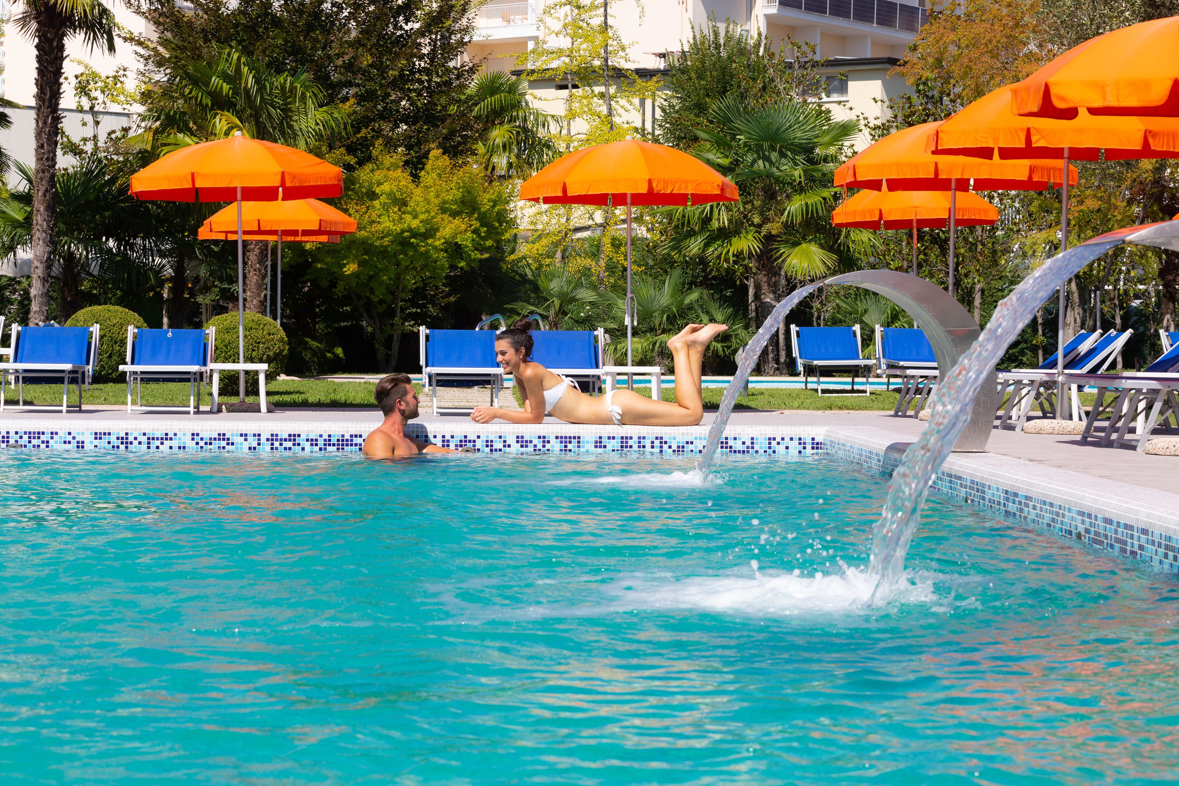 A swimming pool with blue lounge chairs and orange umbrellas.