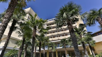 Hotel com vários andares e pátio central rodeado por palmeiras, sob um céu azul límpido.